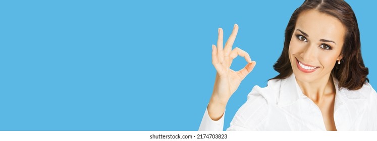 Businesswoman in white confident clothing showing ok hand sign gesture, isolated on blue background. Portrait of happy smiling gesturing brunette woman at studio. Business concept.