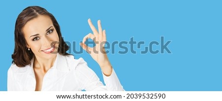 Businesswoman in white confident clothing showing ok hand sign gesture bright blue color background. Portrait of happy smiling gesturing brunette woman at studio Business concept. Female office worker