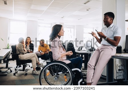 A businesswoman who uses a wheelchair is discussing project and brainstorming whit multicultural colleague at enterprise. A multicultural businesspeople debating about new assignment at office.