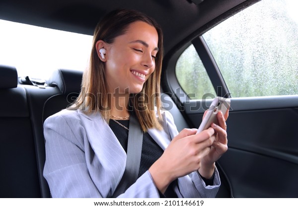 Businesswoman With Wireless Earbuds Commuting To\
Work In Taxi Talking On Mobile\
Phone