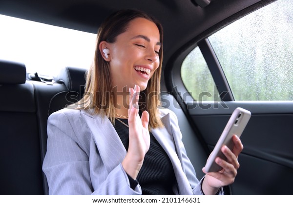 Businesswoman With Wireless Earbuds\
Commuting To Work In Taxi Making Video Call On Mobile\
Phone