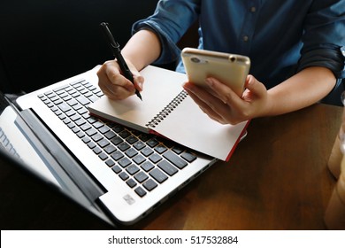 businesswoman work with laptop and phone connect internet for communication, woman hand typing write email and analysis data on wooden table. University life with morning sunlight from window. - Powered by Shutterstock