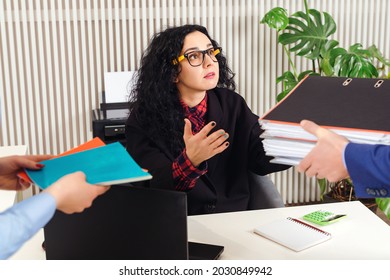 Businesswoman With A Lot Of Work At Workplace. Unfair Chief Giving Assistant Papers And Documents. Stressed Woman Doing Late At Work With A Lot Of Papers, Piles Of Documents, Computer. Office Work