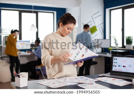 Businesswoman working at her desk in the office checking and analysing report. Executive entrepreneur, manager leader standing working on projects with diverse colleagues.