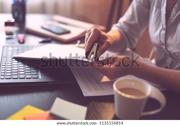 Businesswoman working\
in a home office, removing a staple from a contract, using a staple\
remover. Selective\
focus