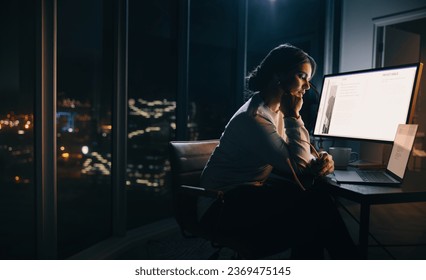 Businesswoman working late in her home office, focusing on a digital marketing project. Woman putting in long hours into her work, sitting with a laptop and a computer screen at her desk. - Powered by Shutterstock