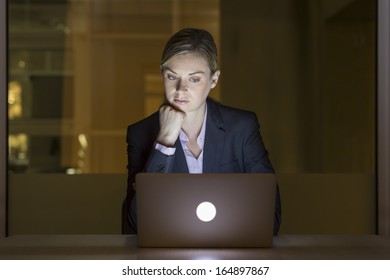 Businesswoman Working Late In Her Office On Laptop, Night Light Building Background 