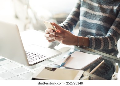 Businesswoman working at office desk and texting with her mobile phone