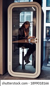 Businesswoman working in phone booth with laptop protect from coronavirus in small closed office