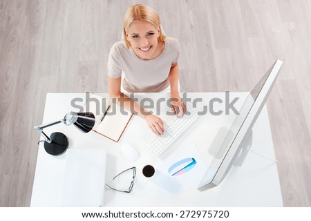 Businesswoman at working place. Top view of beautiful young blond hair woman working at the computer and looking at camera while sitting at her working place