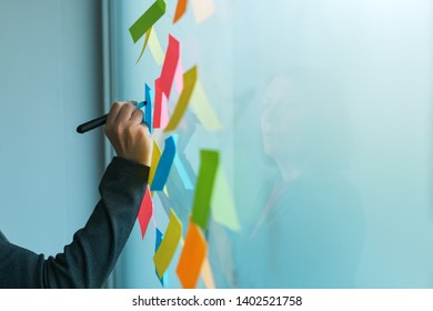 Businesswoman writing on colorful sticky note paper in business office, close up of hand