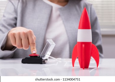 Businesswoman's Hand Launching Rocket By Pressing Red Button
