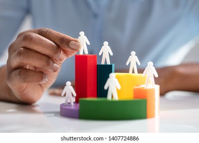 Businesswoman's Hand Placing Human Figures On Multi Colored 3d Pie Chart Over Desk - Powered by Shutterstock