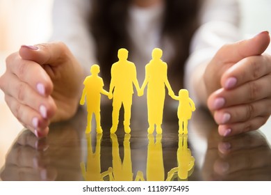 Businesswoman's Hand Protecting Yellow Family Figures Over Desk - Powered by Shutterstock