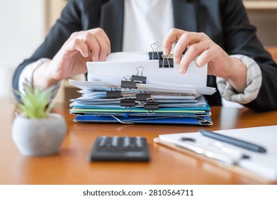 Businesswoman's hands sorting a stack of administrative paperwork, official files, and financial documents with binder clips, showcasing organization and accounting tasks in an office setting