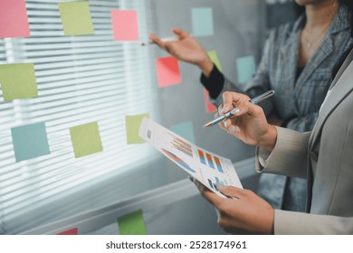 Businesswomen analyzing financial charts and brainstorming using sticky notes in a modern office - Powered by Shutterstock