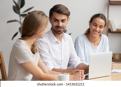 Businesswomen and businessman having pleasant informal talk sitting at office desk in front of computer. Smiling happy diverse coworkers joking, watching funny video during coffee break at work - Powered by Shutterstock