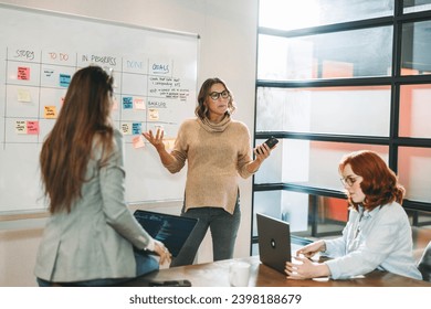 Businesswomen having a collaborative meeting with a scrum master in an office. They brainstorm ideas, discuss software development and project management in a dynamic tech company.