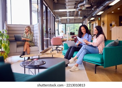 Businesswomen Having Informal Meeting In Breakout Seating Area Of Modern Office