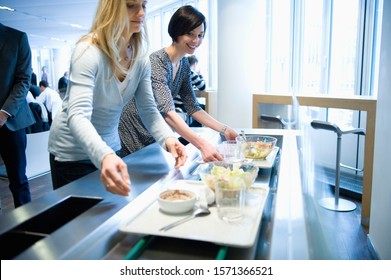 Businesswomen With Lunch Trays In Work Cafeteria