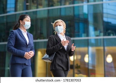 Businesswomen Wearing Office Suits And Masks, Meeting And Walking Together In City, Talking, Discussing Project. Medium Shot. Business During Epidemic Concept