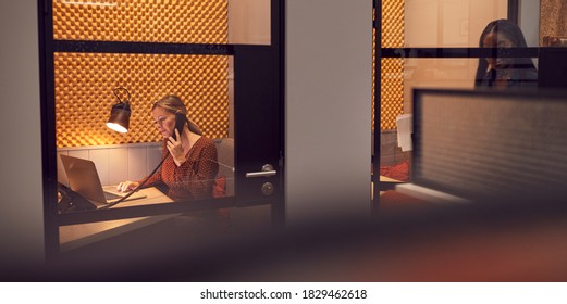 Businesswomen Working Late In Individual Office Cubicles Using Laptop And Digital Tablet