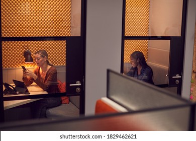 Businesswomen Working Late In Individual Office Cubicles Using Laptop And Digital Tablet