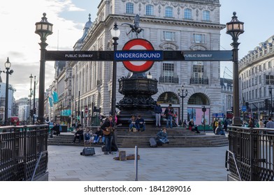 A Busker Playing A Guitar At Piccadilly Circus Under A London Underground Subway Sign On A Sunny Afternoon. London - 26th October 2020