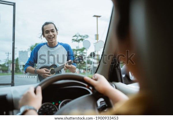 Busker using musical instruments and singing can\
be seen from the front of the windshield when the car is stopped at\
the crossroad traffic\
lights