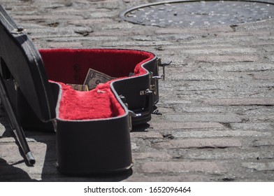 Busking concept. Partial dollar bills visible in busker's guitar case on cobbled street. Selective focus. Copy space.