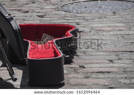 Busking concept. Partial dollar bills visible in busker's guitar case on cobbled street. Selective focus. Copy space.