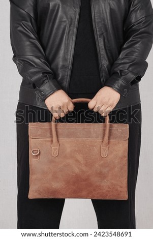 a bussiness woman posing in black leather jacket and brown leather bag 