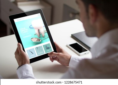 Bussinessman At Office Holding A Tablet Showing Dental Clinic Website. All Screen Graphics Are Made Up.