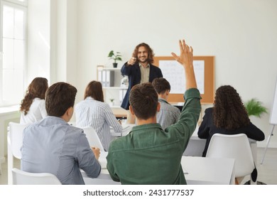 In the bustling school classroom full of students, a dedicated teenage schoolboy raises his hand, signaling active participation during a lesson. The teacher attentively guides the learning process. - Powered by Shutterstock