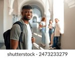 In a bustling university corridor, a young male student with a backpack appears joyful, contrasting with focused classmates in the background, reflecting a dynamic college environment