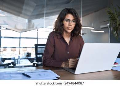 Busy 30s latin hispanic middle age business woman working on laptop computer in office. Focused Indian young businesswoman professional entrepreneur using pc, thinking analysing project at workplace