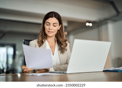 Busy 40 years old business woman working in office checking documents. Mid aged businesswoman accounting manager executive or lawyer using laptop reading paper file financial report, tax invoice.