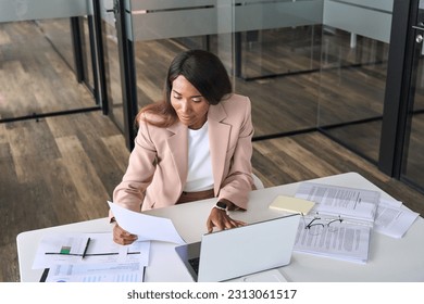 Busy African American business woman professional accountant, marketing manager, financial executive checking document report using laptop checking company papers working sitting at office desk. - Powered by Shutterstock