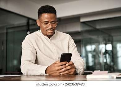 Busy African American entrepreneur using cell phone working in office. Professional young Black business man holding mobile cellphone looking at cellphone making financial bank payment at work. - Powered by Shutterstock