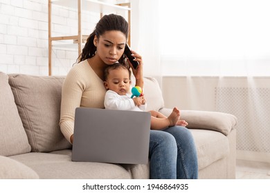 Busy African Mom Working On Laptop Holding Baby Toddler And Talk On Phone Sitting On Couch At Home. Black Mother Works Distantly Caring For Child During Maternity Leave. Freelance Job And Motherhood