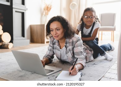 Busy african-american mother freelancer working on distance remotely on laptop, trying to concentrate while her naughty preteen daughter disturbing her. Maternity leave concept. Stay at home