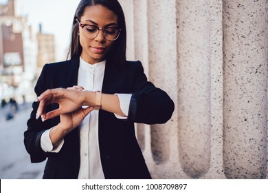 Busy afro American female owner of business company tracking time on smartwatch standing on street near publicity area for financial text.Lawyer with dark skin in formal clothing looking at wristwatch - Powered by Shutterstock