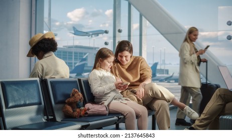 Busy Airport Airplane Terminal: Happy Beautiful Mother and Cute Little Daughter Wait for their Vacation Flight, Use Mobile Smartphone for Fun. Diverse Group of People in Boarding Lounge of Airline Hub - Shutterstock ID 2137645843