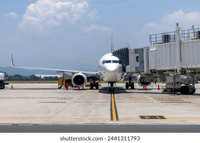 A busy airport tarmac runway with various commercial aircraft planes parked near the terminals, surrounded by airport buildings, structures, and facilities. - Powered by Shutterstock