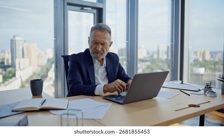 Busy analyst working computer looking papers at corporate workspace closeup. Elderly businessman writing notes creating investment project in office. Tensed manager solving hard issues making decision