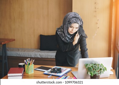 Busy Asian Muslim Business Woman Talking On Mobile Phone And Using Laptop In Modern Office.