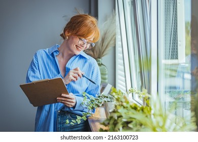 Busy Beautiful Female Florist, Owner Of Small Business Flower Shop, Checking Stocks, Inventory And Data On Clipboard Against Flowers And Plants. Daily Routine Of Running A Small Business