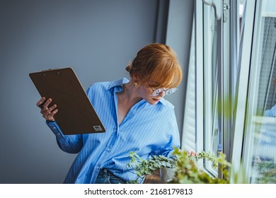 Busy Beautiful Female Florist, Owner Of Small Business Flower Shop, Checking Stocks, Inventory And Data On Clipboard Against Flowers And Plants. Daily Routine Of Running A Small Business