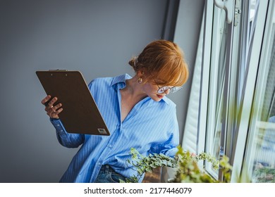 Busy Beautiful Female Florist, Owner Of Small Business Flower Shop, Checking Stocks, Inventory And Data On Clipboard Against Flowers And Plants. Daily Routine Of Running A Small Business