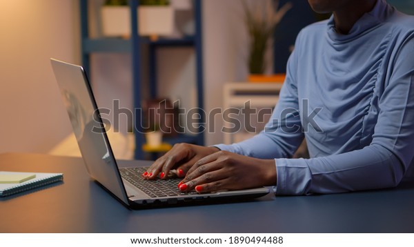 Busy\
black employee typing on computer sitting on chair in modern living\
room office late at night. African entrepreneur working in personal\
workplace writing on keyboard looking at\
desktop